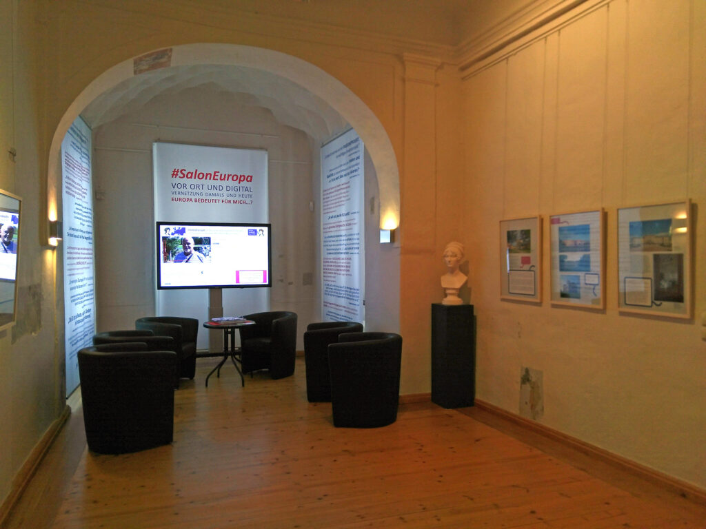 Exhibition with pictures on the walls and a big video screen with interviews